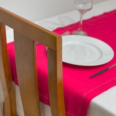 Cadeira de madeira junto a uma mesa com toalha branca e caminho de mesa vermelho com prato, taça e faca