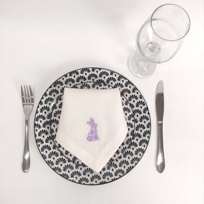 Prato com padrão azul, guardanapo com coelho bordado, talheres em aço e copo transparente