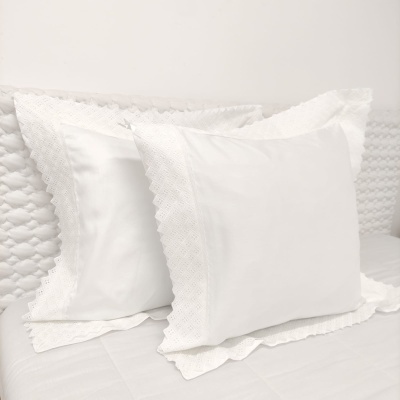 Almofadas brancas com bordas rendadas sobre cama branca acolchoada
