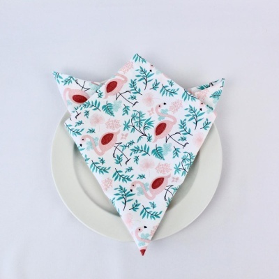 Guardanapo branco com padrão de flamingos e folhas verdes dobrado sobre prato branco