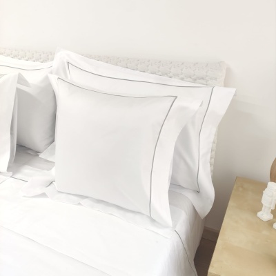 Fronhas e lençol branco com acabamento cinza numa cama minimalista.