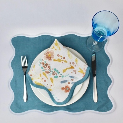 Mesa posta com individual azul, prato branco, guardanapo floral e copo azul