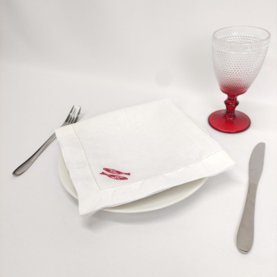 Mesa posta com prato branco, guardanapo com bordado vermelho, garfo, faca e copo com base vermelha.