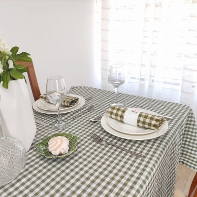 Mesa posta com toalha xadrez verde, pratos brancos, guardanapos xadrez, copos de vinho e vela concha