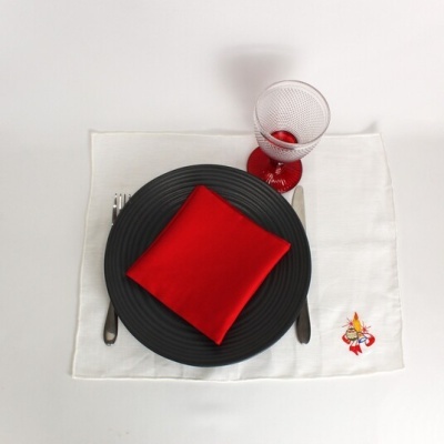 Mesa posta com guardanapo vermelho, prato preto, jogo americano branco bordado e copo com pé vermelho