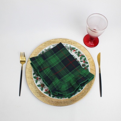 Lugar de mesa com prato decorativo, guardanapo xadrez verde, talheres preto e dourado, copo transparente com base vermelha