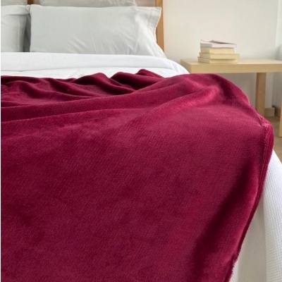 Manta vermelho vinho sobre cama branca com almofadas e mesa de cabeceira