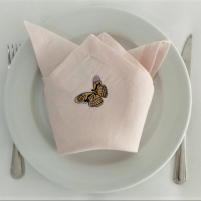 Guardanapo rosa claro com bordado de borboleta em prato branco