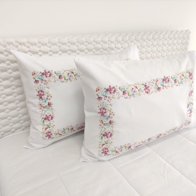 Almofadas brancas com bordado floral colorido sobre cama branca