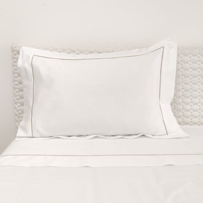 Travesseiro branco com fronha com borda cinza sobre cama branca e cabeceira texturada