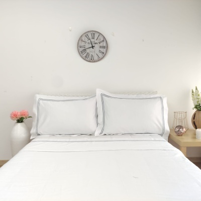 Cama com lençóis brancos e fronhas, relógio de parede e decoração com flores