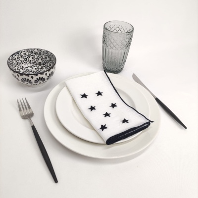 Conjunto de jantar com pratos brancos, taça cinzenta, talheres com cabo preto, guardanapo branco com estrelas e tigela com padrão preto