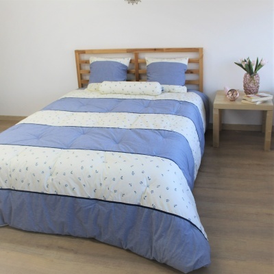 Cama de madeira com roupa de cama azul e branca às riscas com flores e almofadas
