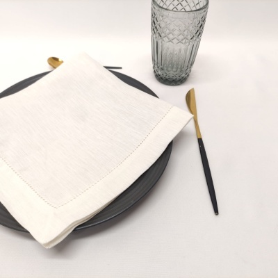 Conjunto de jantar com prato cinza, guardanapo branco, talheres dourados e copo de vidro cinza