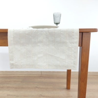 Toalha de mesa branca com linhas verticais sobre mesa de madeira com prato branco e copo de vidro verde.