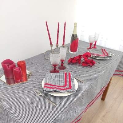 Mesa posta com toalha xadrez preta e branca com detalhes vermelhos, velas e copos decorativos vermelhos