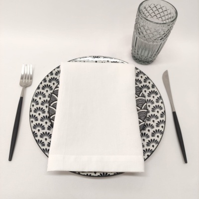 Conjunto de jantar com prato decorado, guardanapo, talheres e copo sobre mesa branca