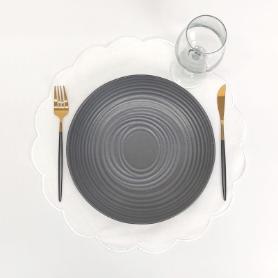 Conjunto de mesa com prato cinzento, talheres preto e dourado, copo transparente e toalha branca em forma de flor