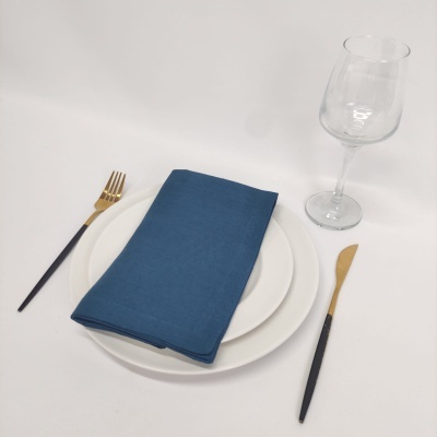 Conjunto de jantar com pratos brancos, guardanapo azul, talheres preto e dourado e copo de vidro.