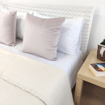 Cama com cabeceira branca e almofadas castanhas claras, mesa de cabeceira ao lado com livros e vaso decorativo