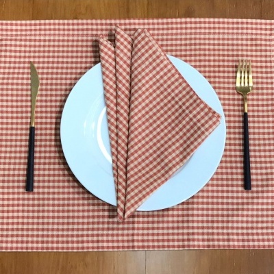 Toalha individual e guardanapo xadrez laranja e branco, prato branco, talheres com detalhes dourados sobre mesa de madeira