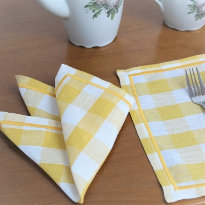 Guardanapos xadrez amarelo e branco em mesa de madeira com jarros brancos ao fundo