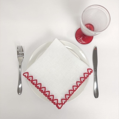 Conjunto de mesa com prato branco, guardanapo bordado, talheres metálicos e copo com pé vermelho