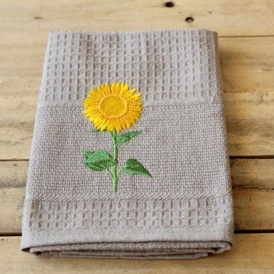 Toalha cinzenta com bordado de girassol sobre madeira clara