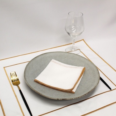 Conjunto de mesa com prato cinzento, guardanapo branco, talheres dourados e copo de vidro