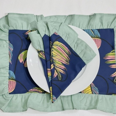 Conjunto de mesa com placemat verde claro, guardanapo e sousplat com padrão de folhas coloridas e prato branco