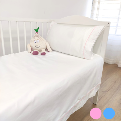 Cama infantil branca com roupa de cama branca e detalhes cor-de-rosa e peluche sentado no colchão