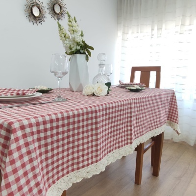 Toalha xadrez vermelho e branco com renda creme sobre mesa de madeira com decoração floral e vidro