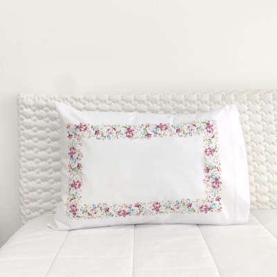 Travesseiro branco com fronha bordada com flores coloridas sobre cama branca com cabeceira creme