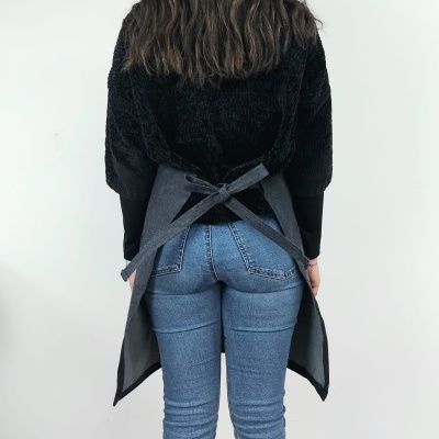 Pessoa de costas usando avental cinzento com laço e roupa preta e jeans azul claro
