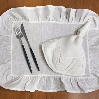 Lugar posto com individual branco, guardanapo com laço e talheres com cabos pretos sobre mesa de madeira.