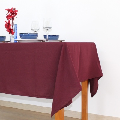 Toalha de mesa bordeaux em mesa de madeira com pratos azuis e vaso azul com flores vermelhas