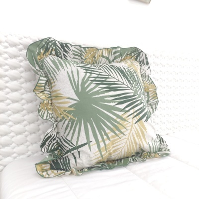 Almofada quadrada com padrão de folhas verdes e amarelas com folhos na borda sobre fundo branco
