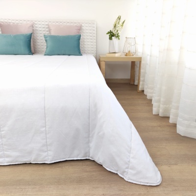 Cama com edredão branco e almofadas azuis e rosa junto a mesa de cabeceira com vaso e flores