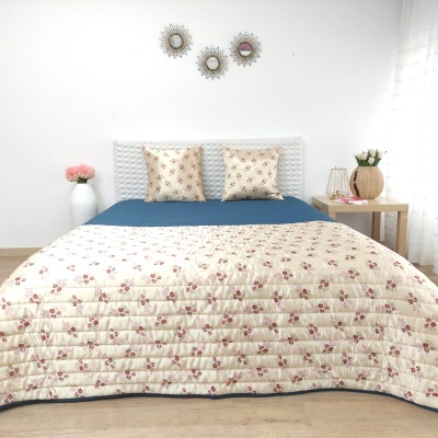 Quarto com cama e decoração simples, destacando a colcha floral creme com vermelho e azul.