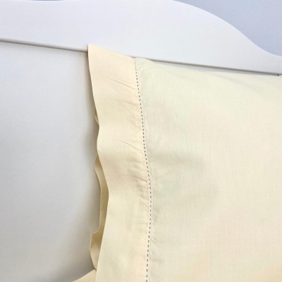 Fronha creme com babado numa cama branca