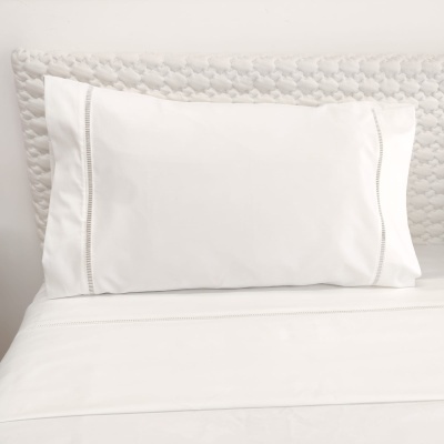 Travesseiro branco com fronha decorativa sobre cama com lençóis brancos e cabeceira texturizada