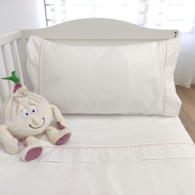 Berço branco com roupa de cama branca e almofada com bordado rosa e peluche em forma de alho