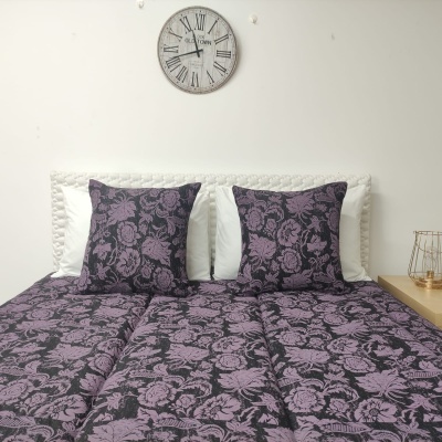 Cama com colcha e almofadas florais roxas e pretas, almofadas brancas, relógio de parede e mesa de cabeceira