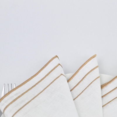 Guardanapo branco com riscas douradas e garfo num fundo branco