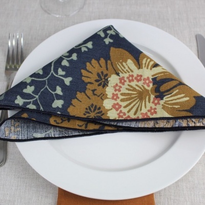 Guardanapo de tecido com padrão floral em azul, castanho e bege sobre prato branco