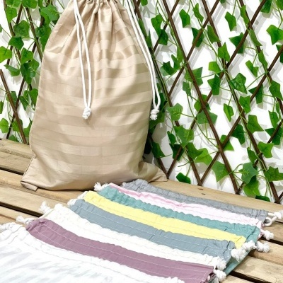 Sacolas de pano coloridas em tons pastel alinhadas sobre madeira com saco bege e treliça verde ao fundo