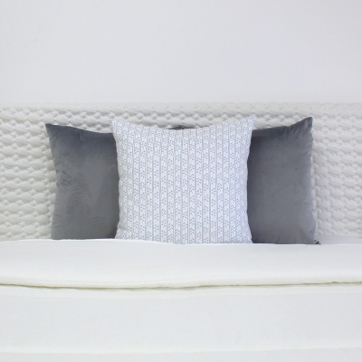 Cama com almofadas cinza e branca com padrão azul na cabeceira branca acolchoada