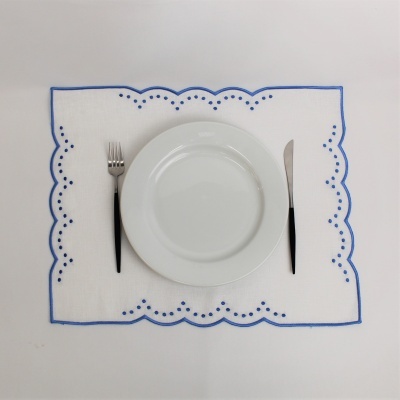 Jogo americano branco com borda azul e talheres ao lado de um prato branco