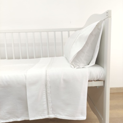 Cama branca de madeira com lençol e fronha brancos com detalhe decorativo