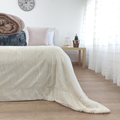 Cama com colcha creme macia e acessórios num quarto branco e soalheiro